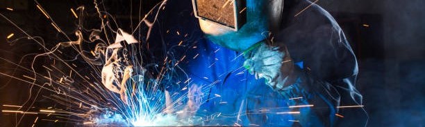 作業者が溶接トーチを持ち溶接を行い、火花を散らしている様子